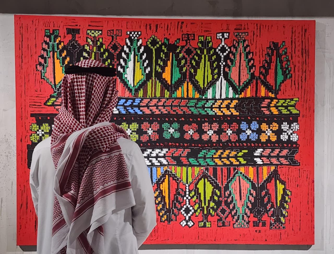 زائر يقف أمام قطعة مطرّزة يدويّاً من التراث الفلسطيني